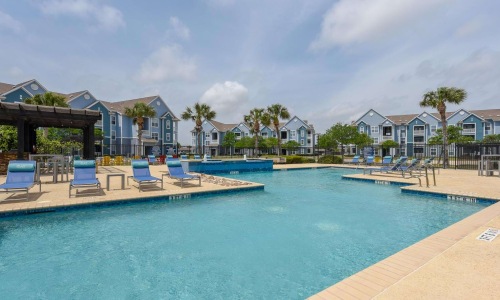 a pool with chairs and tables by it and houses in the background